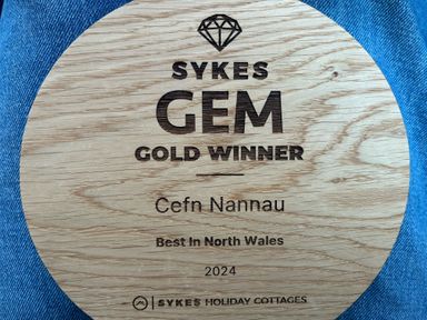 A wooden circular plaque awarded to Cefn Nannau for being the best in North Wales in 2024 placed on blue denim fabric