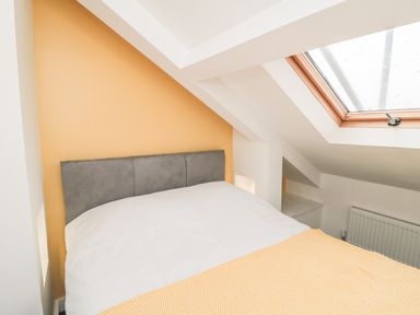 A bedroom with a bed under a skylight and a yellow accent wall at 11A Church Street in Whitby