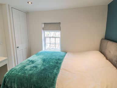A bedroom with a bed covered with a green blanket and white sheet next to a window and a white door at 11A Church Street in Whitby