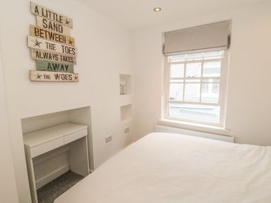 A bedroom with a white bed, a small white desk in a wall recess, a window with a blind, and a wall sign at 11A Church Street Whitby