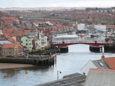 A river with a red bridge crossing it surrounded by houses and boats at 11A Church Street in Whitby