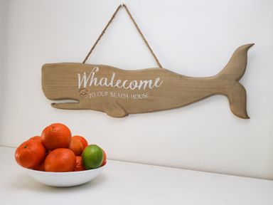 A wooden whale-shaped sign with the text Welcome to our beach house and a bowl of oranges and a lime on a white surface at 11A Church Street in Whitby