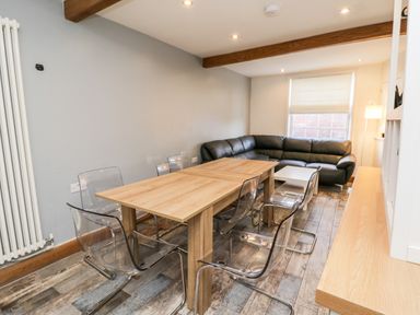 A dining area with a wooden table surrounded by transparent chairs and a black leather sectional sofa at 11A Church Street in Whitby