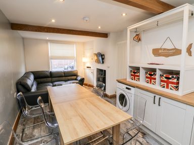 A living room with a wooden dining table surrounded by clear chairs and a black leather sofa at 11A Church Street in Whitby