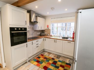 A kitchen with white cabinets wooden countertops a colorful rug and a window at 11A Church Street in Whitby