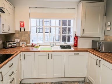 A kitchen with white cabinets wooden countertops a sink toaster microwave and a window at 11A Church Street Whitby