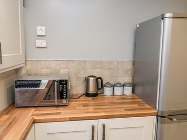 A kitchen corner with a microwave, electric kettle, three labeled canisters, and a refrigerator at 11A Church Street in Whitby