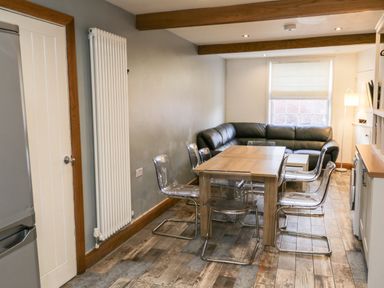 A dining area with wooden table transparent chairs black corner sofa and window at 11A Church Street Whitby
