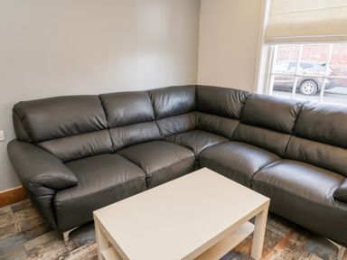 A corner black leather sofa with a white coffee table in front and a window showing a parked car outside at 11A Church Street in Whitby