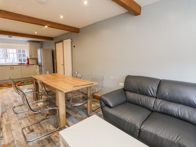 A dining area with a wooden table and transparent chairs next to a black leather sofa and a kitchen in the background at 11A Church Street Whitby