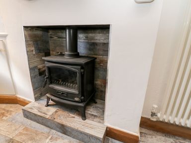A black wood burning stove set in a tiled fireplace with a white wall and radiator nearby at 11A Church Street in Whitby