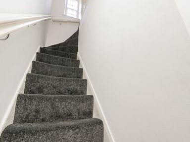 A staircase with dark carpet and white walls with a window at the top at 11A Church Street in Whitby