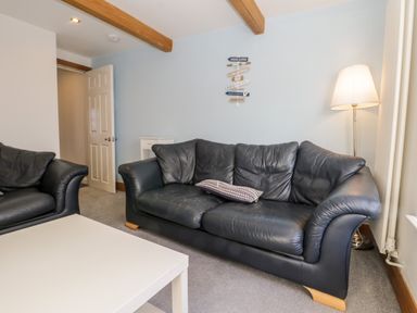 A living room with black leather sofas a white coffee table a floor lamp and a sign on the wall at 11A Church Street in Whitby