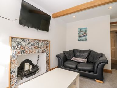 A living room with a black leather sofa a white table a tiled fireplace with candles and a wall mounted television at 11A Church Street in Whitby