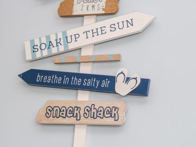 A wall with wooden directional signs including soak up the sun breathe in the salty air and snack shack at 11A Church Street in Whitby