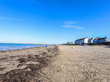 A sandy beach with seaweed patches people near water and buildings along the shore at Tides Reach in Rhosneigr