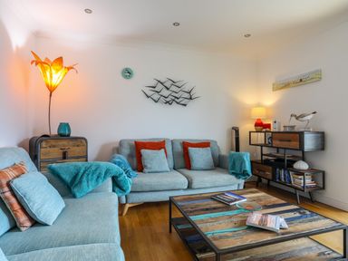 A living room with blue sofas red and blue cushions a wooden coffee table and decorative lamps at Tides Reach in Rhosneigr