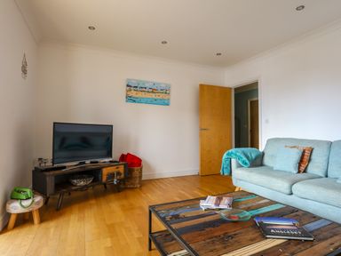 A living room with a television on a wooden stand and a blue sofa with cushions and a throw at Tides Reach in Rhosneigr