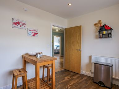 A dining area with a wooden table and stools near an open door showing a bedroom at Tides Reach in Rhosneigr