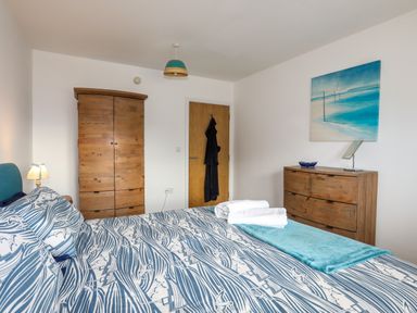 A bedroom with a bed with patterned bedding wooden wardrobe wooden chest of drawers and a painting on the wall at Tides Reach in Rhosneigr