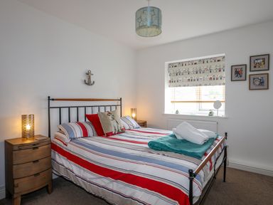 A bedroom with a double bed with striped bedding and bedside tables with lamps at Tides Reach in Rhosneigr