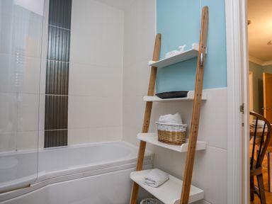 A bathroom with a bathtub and a wooden shelf with towels and a basket at Tides Reach in Rhosneigr