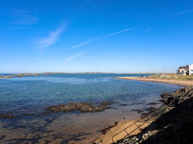 A coastal scene with sandy beach rocks and houses near the shore at Tides Reach in Rhosneigr