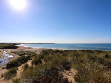 A sandy beach with grass-covered dunes and a small stream flowing into the sea at Tides Reach in Rhosneigr