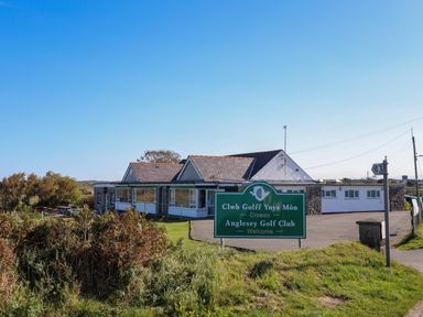 A building with a sign for Anglesey Golf Club in front with grass and bushes around at Tides Reach in Rhosneigr
