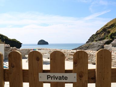 A wooden fence with a private sign overlooking a terrace with a white picnic table and ocean view at Gull Rock in Trebarwith Strand