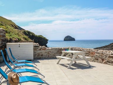 A patio with blue lounge chairs and a white picnic table overlooking the sea at Gull Rock in Trebarwith Strand