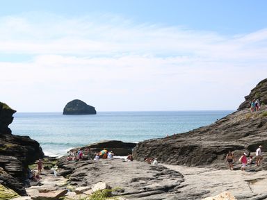 A rocky seaside area with people sitting and walking near the ocean at Gull Rock in Trebarwith Strand