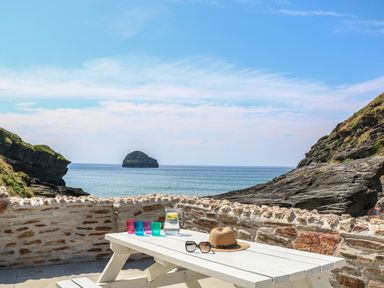 A picnic table with colorful glasses a jug of water a hat and sunglasses with a sea view at Gull Rock in Trebarwith Strand