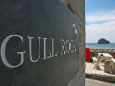 A sign with Gull Rock text on a wall near an outdoor seating area and ocean view at Gull Rock in Trebarwith Strand
