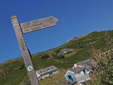 A wooden signpost for a coast path footpath on a hill with houses and flowers at Gull Rock in Trebarwith Strand