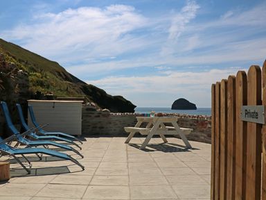 An outdoor patio with blue lounge chairs and a white picnic table near the sea at Gull Rock in Trebarwith Strand