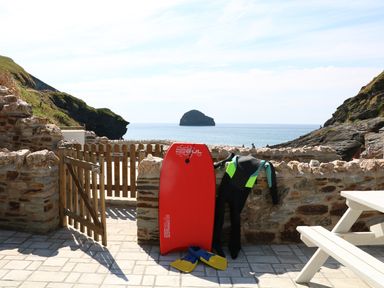 A stone patio with a wooden gate a red bodyboard a wetsuit and fins overlooking the sea at Gull Rock in Trebarwith Strand