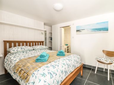 A bedroom with a wooden bed with sailboat print bedding teal towels on the bed a chair with a cushion and a beach painting on the wall at Gull Rock in Trebarwith Strand