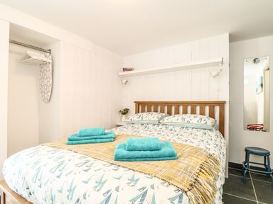 A bedroom with a wooden bed, patterned bedspread, towels on a yellow throw, an ironing board, a stool and a wall mirror at Gull Rock in Trebarwith Strand