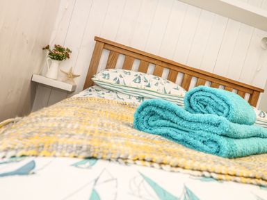 A bed with sailboat patterned sheets and folded blue towels at Gull Rock in Trebarwith Strand