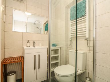A bathroom with a sink cabinet toilet glass shower and shelves at Gull Rock in Trebarwith Strand
