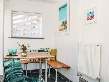 A small dining area with a wooden table and bench with cushions next to a window with blinds at Gull Rock in Trebarwith Strand