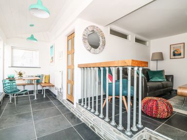 A room with a small dining area with bench seating and a table and a living area with armchairs a leather sofa and a knitted pouf at Gull Rock in Trebarwith Strand