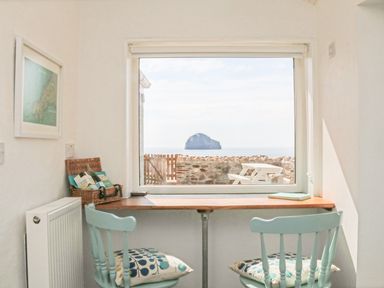 A small room with two blue chairs and a wooden desk by a large window overlooking a sea view and a stone wall at Gull Rock in Trebarwith Strand