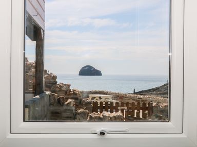 A sea view through a window with rocks a wooden fence and a picnic table at Gull Rock in Trebarwith Strand