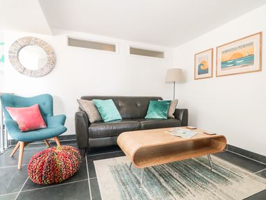 A living room with a black sofa teal armchair wooden coffee table and wall art at Gull Rock Trebarwith Strand