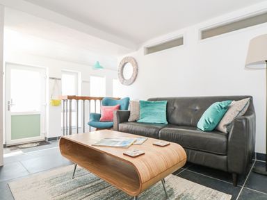 A living room with a black sofa with pillows a wooden coffee table and a blue armchair at Gull Rock in Trebarwith Strand