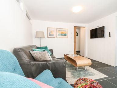 A living room with a leather sofa blue armchair wooden coffee table and wall mounted television at Gull Rock in Trebarwith Strand