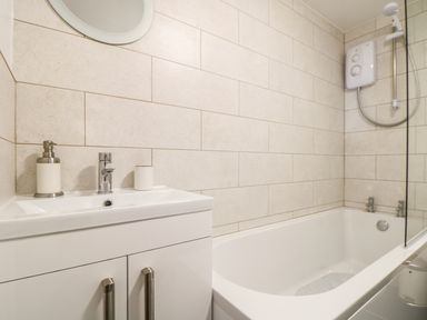 A bathroom with a white sink cabinet soap dispenser and a bathtub with shower at Gull Rock in Trebarwith Strand