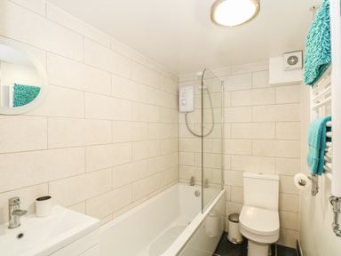 A bathroom with a bathtub shower combination a toilet a sink and turquoise towels at Gull Rock in Trebarwith Strand